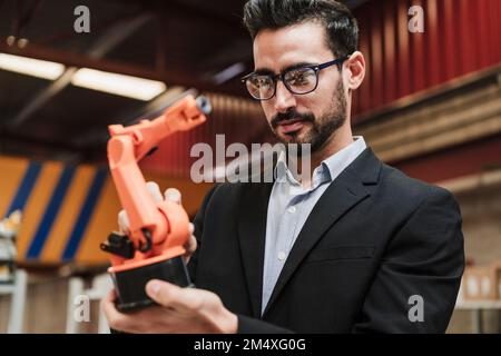 Businessman wearing eyeglasses examining robotic arm at industry Stock Photo