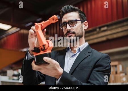 Businessman wearing eyeglasses examining robotic arm at factory Stock Photo