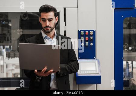 Engineer using laptop standing in front of machinery Stock Photo