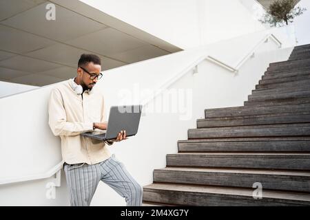 Freelancer using laptop standing at staircase Stock Photo