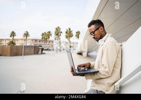 Freelancer using laptop leaning by wall Stock Photo