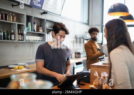 Smiling barista using tablet PC at counter in cafe Stock Photo
