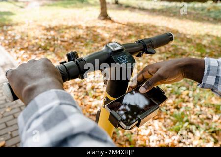Man using mobile app on electric push scooter Stock Photo