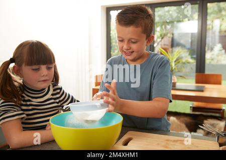 Smiling boy sieving flour by sister at home Stock Photo