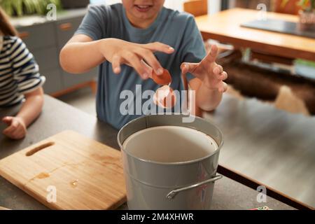 Hand of boy throwing egg shell in garbage bin at home Stock Photo