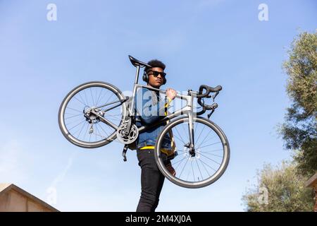Young man carrying bicycle under clear blue sky Stock Photo