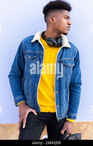Young man wearing denim jacket standing in front of wall Stock Photo