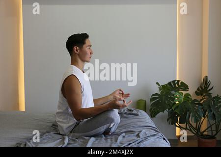 Young man practicing yoga sitting on bed at home Stock Photo