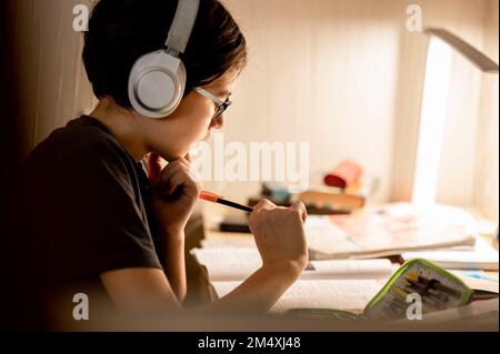 Boy wearing wireless headphones doing homework at home Stock Photo