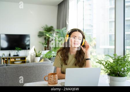 Smiling freelancer wearing wireless headphones looking at laptop Stock Photo