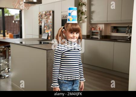 Smiling girl standing with plastic container on head at home Stock Photo
