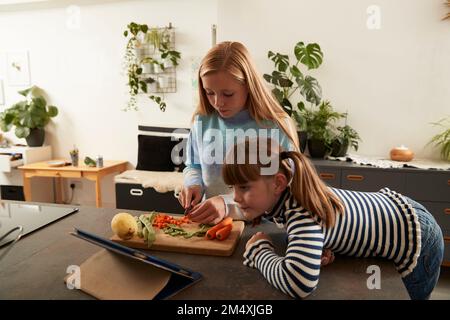 Girl preparing food with sister using tablet PC at home Stock Photo