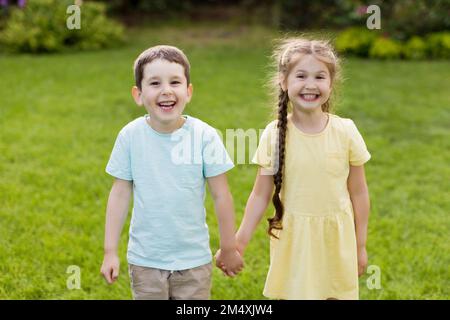 Cheerful brother and sister holding hands standing in garden Stock Photo