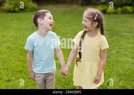 Brother and sister holding hands and laughing together in back yard Stock Photo