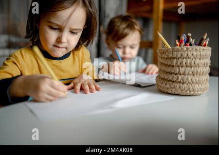 Boy with brother drawing on paper by colored pencils in jute container Stock Photo