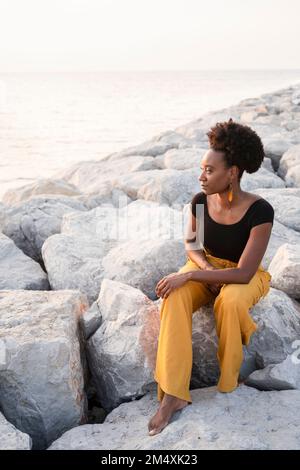 Woman sitting on rocks and looking at sea Stock Photo