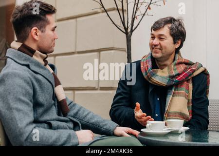 Happy father and son sitting with coffee cups at sidewalk cafe Stock Photo