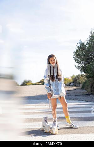 Girl holding white roller skate on zebra crossing Stock Photo