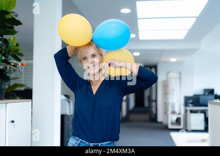 Happy businesswoman holding balloons in office Stock Photo