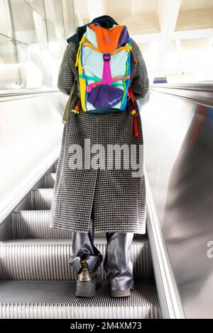 Rear back vertical view of a young woman with colourful rucksack standing on escalator of Elizabeth Line underground London England UK   KATHY DEWITT Stock Photo