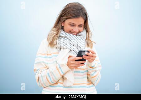 Smiling blond young woman using smart phone at beach Stock Photo