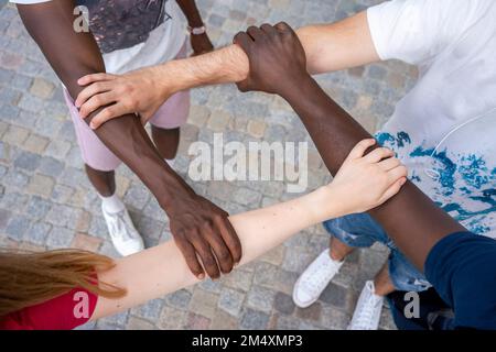 Multiracial friends holding hands together standing on footpath Stock Photo