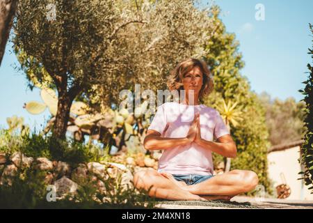 Smiling mature woman with hands clasped meditating in back yard Stock Photo
