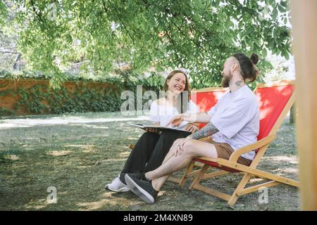 Happy couple with book sitting on deck chairs in backyard Stock Photo