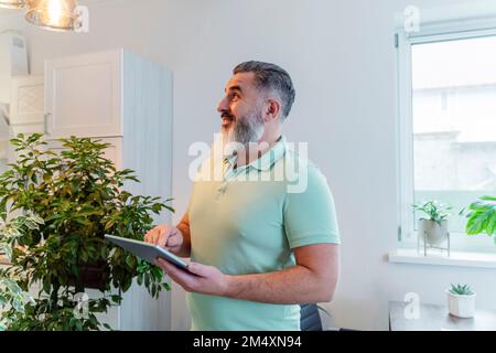Smiling man with tablet PC looking at illuminated bulb in home Stock Photo