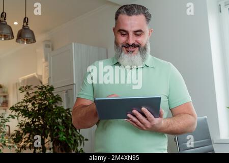 Smiling mature bearded man using tablet PC at home Stock Photo