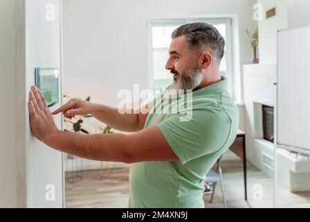 Smiling man using smart home application through tablet PC mounted on wall Stock Photo