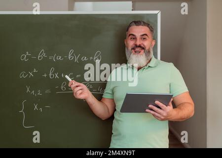 Mature teacher with tablet PC teaching mathematics on chalkboard Stock Photo