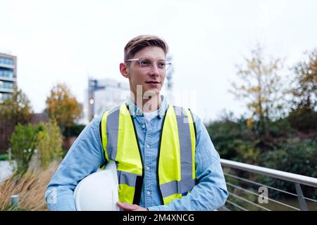 Contemplative engineer wearing eyeglasses holding hardhat under arm Stock Photo