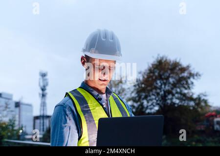 Engineer wearing hardhat using laptop Stock Photo