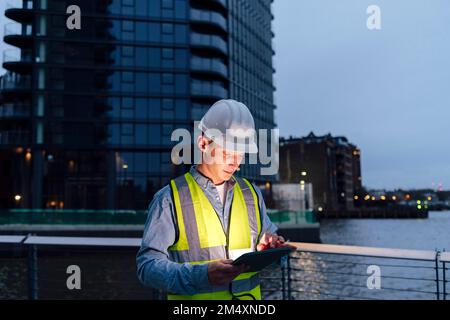 Engineer wearing hardhat using tablet PC by railing Stock Photo