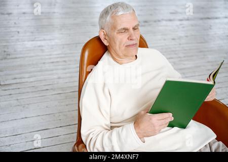 Man reading book sitting on chair at home Stock Photo