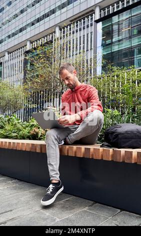 Man using laptop on bench Stock Photo