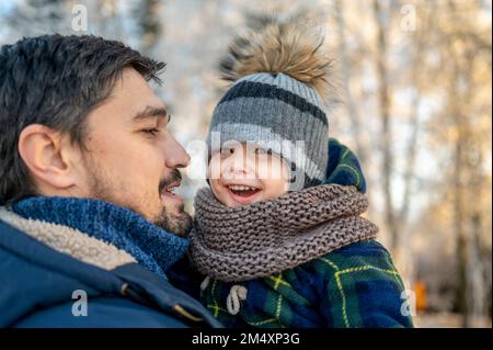 Father carrying happy son wearing knit hat in winter Stock Photo