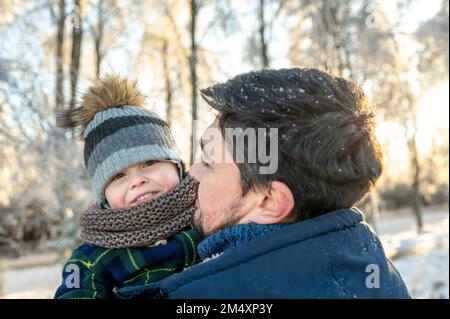 Smiling boy with father wearing warm clothing in winter park Stock Photo