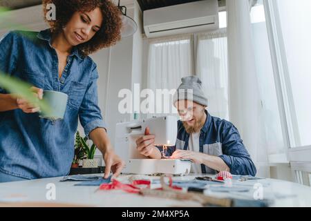 Fashion designer working on sewing machine with colleague examining fabric in workshop Stock Photo