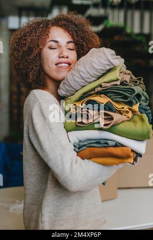Smiling young fashion designer standing with clothes in workshop Stock Photo