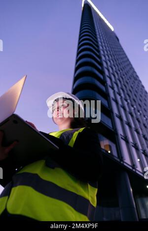 Smiling engineer using laptop in front of building at dusk Stock Photo