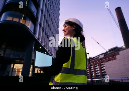 Smiling young engineer holding laptop at dusk Stock Photo