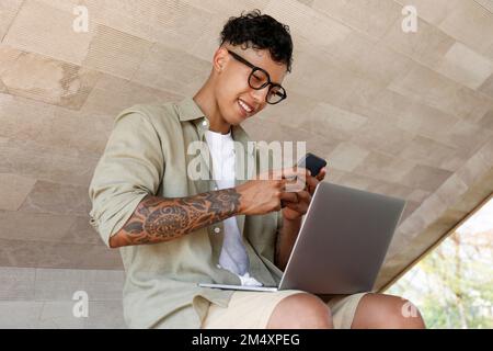 Happy freelancer using smart phone sitting with laptop Stock Photo