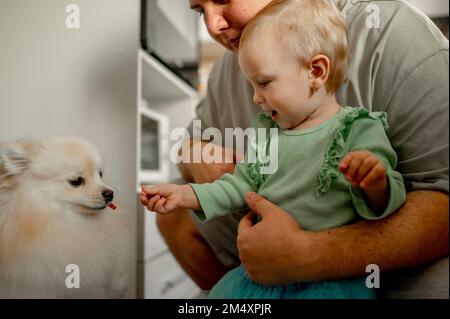 Father with cute daughter feeding dog at home Stock Photo