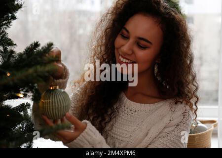 Happy woman decorating Christmas tree with bauble at home Stock Photo