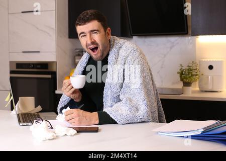 Sleepy looking man working from a cold home office Stock Photo