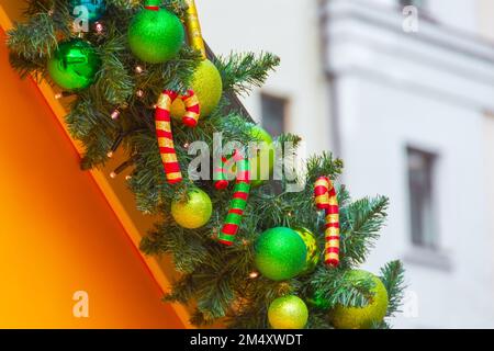 New Year and Christmas decorations with spruce branches, shiny balls, striped sweets along the perimeter of the roof, against the backdrop of houses Stock Photo