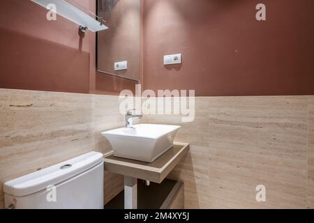 small toilet with deep white porcelain sink on wooden furniture and marble tiles Stock Photo