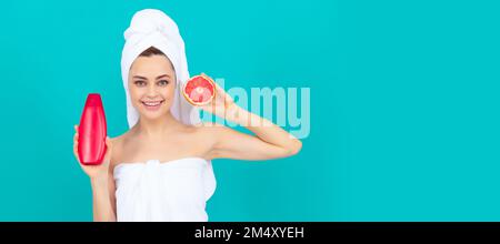 happy beautiful woman in towel with grapefruit shampoo bottle on blue background. Beautiful woman isolated face portrait, banner with mock up copy Stock Photo